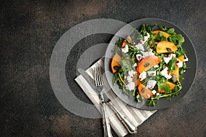 Healthy salad with persimmons, arugula, feta cheese and pumpkin seeds on a dark plate