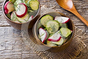 Healthy salad with radishes and cucumbers in a wooden bowl.