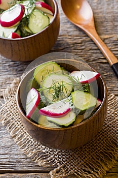 Healthy salad with radishes and cucumbers in a wooden bowl.