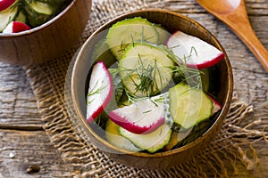 Healthy salad with radishes and cucumbers in a wooden bowl.