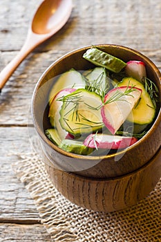 Healthy salad with radishes and cucumbers in a wooden bowl.