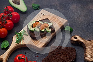 Healthy sandwich with avocado, tomatoes and spices on whole grain bread. Wooden cutting boards on a dark background
