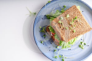 Healthy sandwich with gluten-free bread, tomato, lettuce and germinated microgreens, sprinkled with sesame seeds served in plate