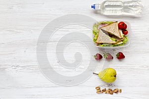 Healthy school lunch box with fresh fruits, walnuts, organic vegetables sandwiches and bottle of water on white wooden background,