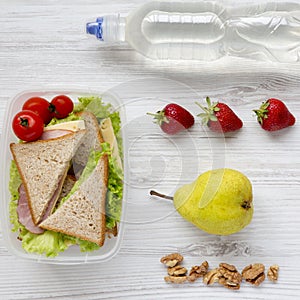 Healthy school lunch box with fresh fruits, walnuts, organic vegetables sandwiches and bottle of water on white wooden background,