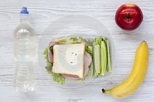 Healthy school lunch box with fresh organic vegetables sandwich, fruits and bottle of water on white wooden background, flat lay.