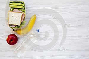 Healthy school lunch box with fresh organic vegetables sandwich, fruits and bottle of water on white wooden background, flat lay.