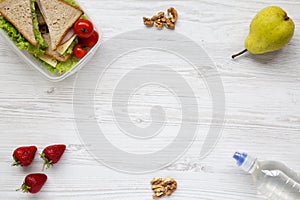 Healthy school lunch box with fresh organic vegetables sandwiches, walnuts, bottle of water and fruits on white wooden background,