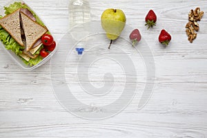 Healthy school lunch box with fresh organic vegetables sandwiches, walnuts, bottle of water and fruits on white wooden background,