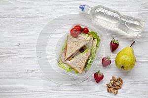 Healthy school lunch box with fresh organic vegetables sandwiches, walnuts, bottle of water and fruits on white wooden background,