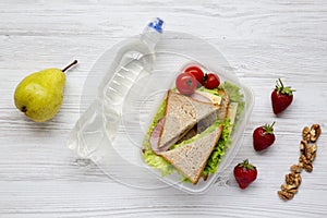 Healthy school lunch box with fresh organic vegetables sandwiches, walnuts, bottle of water and fruits on white wooden background,