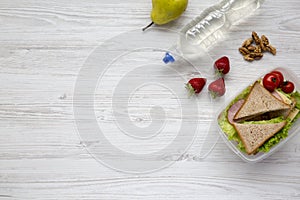 Healthy school lunch box with fresh organic vegetables sandwiches, walnuts, bottle of water and fruits on white wooden background,