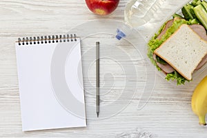 Healthy school lunch box with notebook and pencil on white wooden background, flat lay. From above.