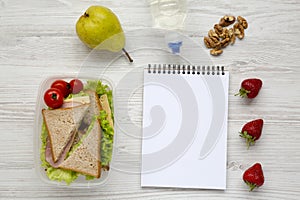 Healthy school lunch box with notebook on white wooden background, flat lay. From above.