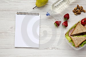 Healthy school lunch box with notebook on white wooden background, flat lay. From above. Top view.