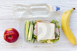 Healthy school lunch box with sandwich, fruits and bottle of water on white wooden background, flat lay. From above.