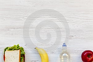 Healthy school lunch box with sandwich, fruits and bottle of water on white wooden background, flat lay. From above. Copy space.