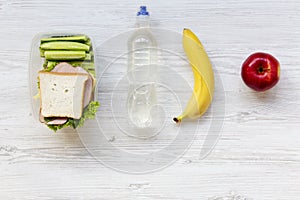 Healthy school lunch box with sandwich, fruits and bottle of water on white wooden background, top view. From above.