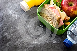 Healthy school lunch box: Sandwich, vegetables ,fruit and juice on black stone.