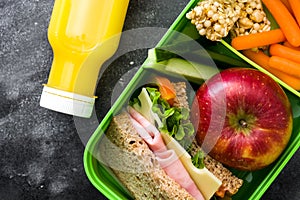 Healthy school lunch box: Sandwich, vegetables ,fruit and juice on black stone.