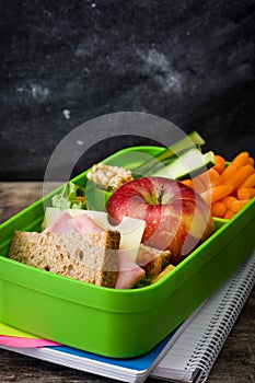 Healthy school lunch box: Sandwich, vegetables, fruit, juice and water on wood