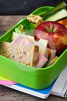 Healthy school lunch box: Sandwich, vegetables, fruit, juice and water on wood