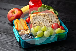 Healthy school, work lunch box with sandwiches and fresh vegetables, nuts, bottle of juicy and fruits on wooden table