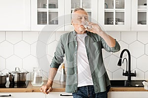 Healthy senior man drinking glass of water in his kitchen