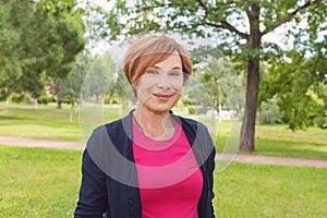 Healthy senior woman walking in park. Older woman with red short haircut outdoors. Mature beauty, 60s