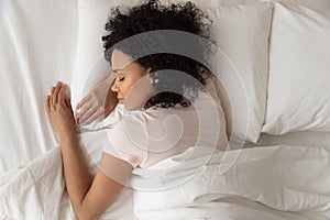 Healthy serene african girl sleeping in comfortable bed, top view