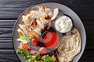 Healthy shawarma plate with chicken, hummus, salad and sauces close-up on a table. Horizontal top view photo