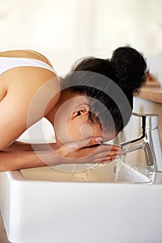 Healthy skin starts with healthy habits. a young woman washing her face at the bathroom sink.