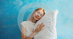 Healthy sleep, happy relaxed sleepy young woman on white soft comfortable pillow imagining she lying on the bed on blue sky with