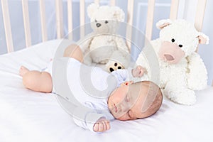 Healthy sleep of a newborn baby in a crib in the bedroom with a soft toy bear on a cotton bed