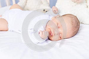 Healthy sleep of a newborn baby in a crib in the bedroom with a soft toy bear on a cotton bed