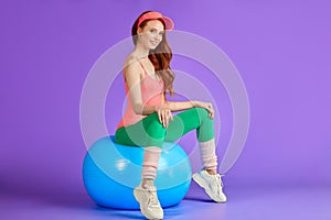 Healthy slim ginger girl sits relaxed on fitness ball, hands on knees