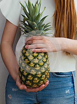 Healthy slim girl with long red hair holding a pineapple