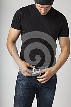 Healthy, slim, slender young man wearing black t-shirt, jeans and knit hat putting on a belt fastening buckle. Young men`s modern