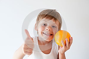 Healthy small smiling kid holding orange fruit and thumb up on white background