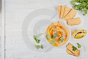 Healthy snack from crispbread with hummus, olive oil and cillantro on white wooden background