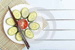 Healthy snack from sliced tomato and cucumber on wooden table. Bamboo mat with chopsticks. Top view. Copy space