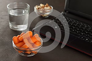 Healthy snacks for workplace lunch: baby carrots, almonds, cashew and glass of water.