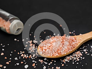 Healthy spices concept. Large dark pink himalayan salt in a wooden spoon and spilled on a black table. Closeup