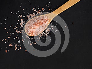 Healthy spices concept. Large dark pink himalayan salt in a wooden spoon and spilled on a black table. Closeup