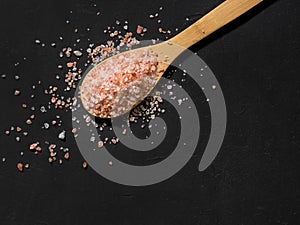 Healthy spices concept. Large dark pink himalayan salt in a wooden spoon and spilled on a black table. Closeup