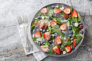 Healthy Spinach salad with berries such as strawberries, blueberries with cheese and pecans and honey dressing close-up in a plate