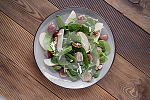 Healthy spinach salad made with red apple, wallnuts, grapes. Wooden rustic background, top view