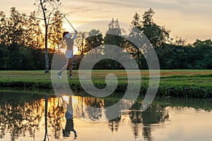 Healthy Sport. Asian Sporty woman golfer player chips and swing golf on the green sunset evening time, she presumably does exercis