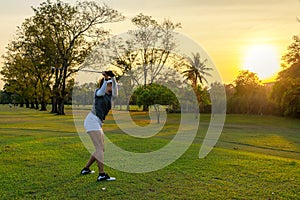Healthy Sport. Asian Sporty woman golfer player doing golf swing tee off on the green course evening time, she presumably does exe