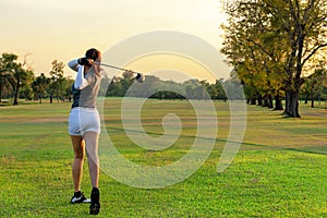 Healthy Sport. Asian Sporty woman golfer player doing golf swing tee off on the green evening time,